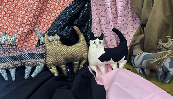 Four fabric cats standing in front of a fabric background