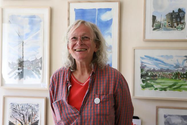 Artist Jo Dunn stands in front of her framed artworks of landscapes