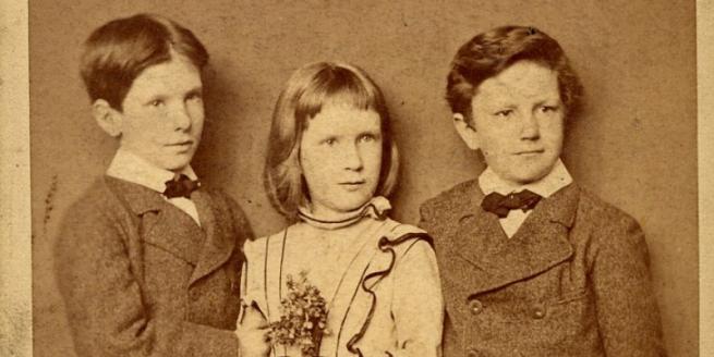 Three children in period outfits looking beyond the camera.