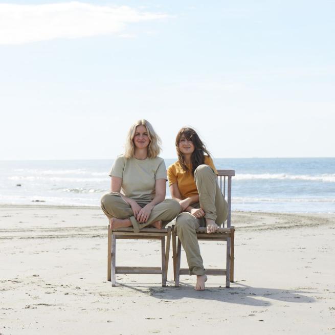 Lizzy and Catherine Ward Thomas sat next to each other on wooden garden chairs on a beach.