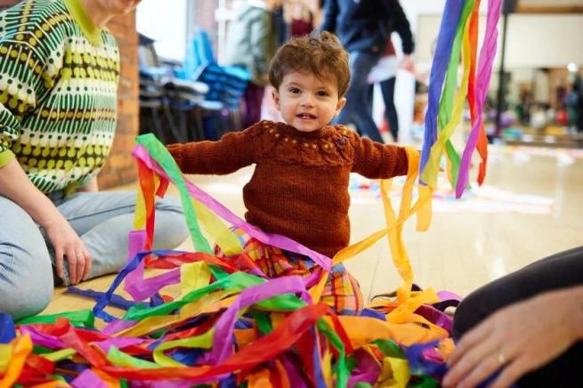 Toddler looks at the camera whilst playing with colourful string.
