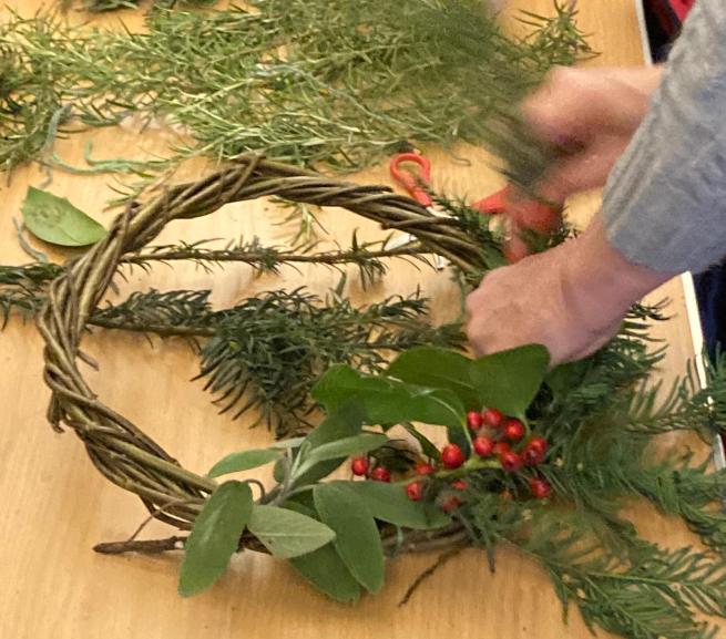 A picture of someone making a festive wreath from foraged foliage, with the person's hands on view.