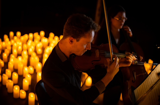 A man playing violin in front of candles, creating a serene and intimate atmosphere.