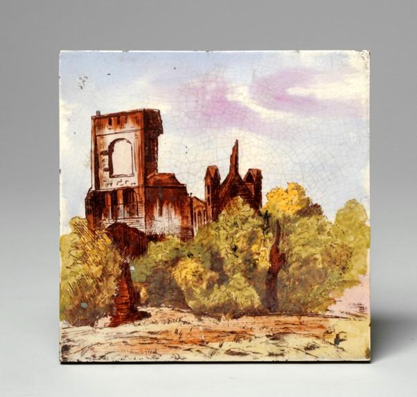 A ceramic tile with a picture of a ruin (Kirkstall Abbey) surrounded by trees against a backdrop of clouds.