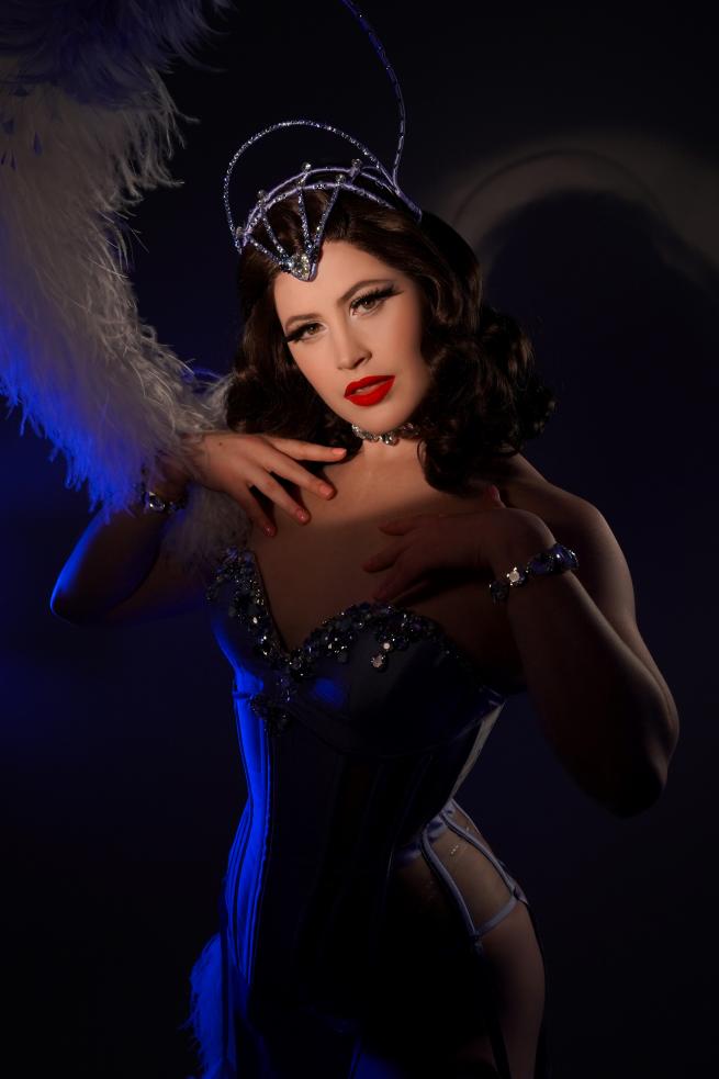 Glamorous showgirl with brunette hair, wearing an ostrich feather headpiece, corset and rhinestones.