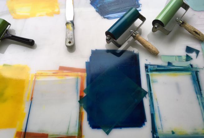Image shows navy blue and yellow inks rolled across the surface of a white table and some rollers covered in ink.