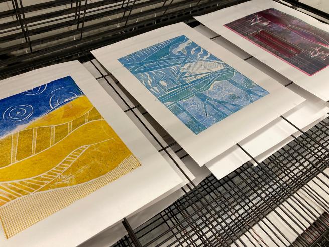 Image shows some colourful prints laying on a print drying rack.