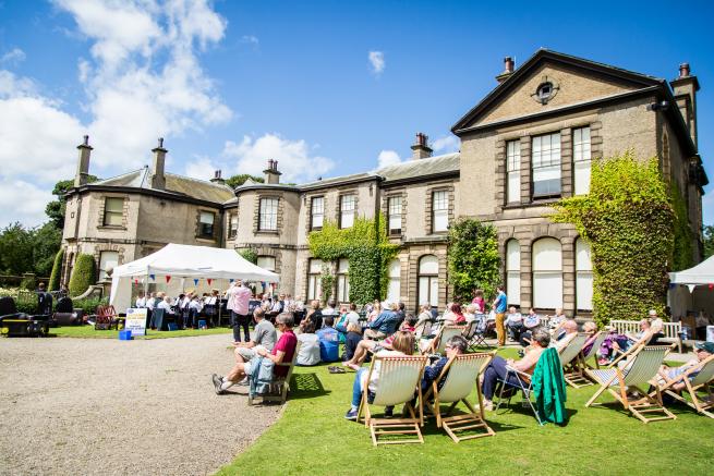 Image of people on deckchairs sat and stood outside a Edwardian stately home.
