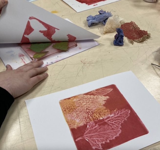 Somebody creating a monoprint of leaves using a gelli plate and red ink