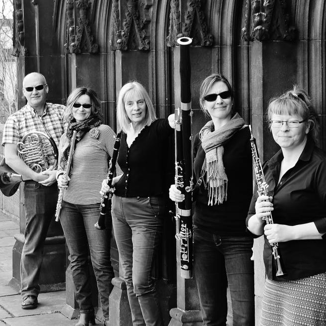 Sospiri wind quintet are looking at the camera holding their instruments, a flute, oboe, clarinet, bassoon and horn and the image is in black and white.
