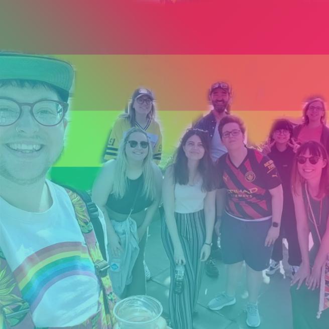 A group of people smile at the camera with a rainbow pride background