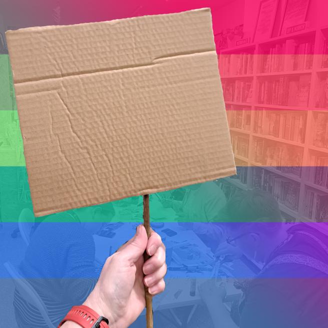 A white hand holds a cardboard sign against a rainbow coloured backdrop