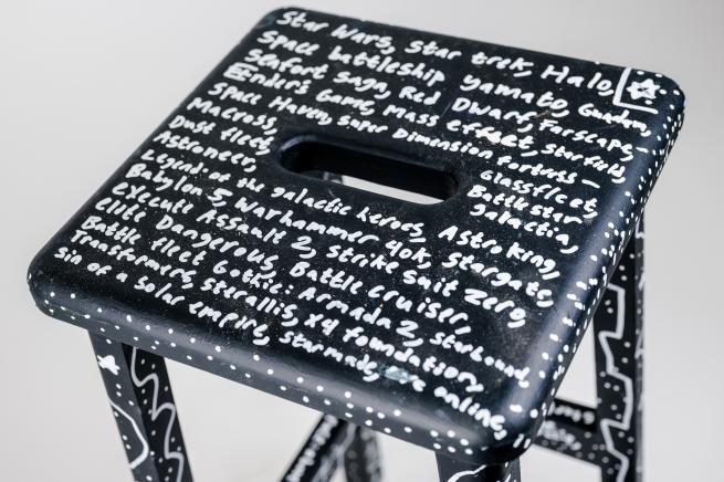 A stool, painted black with dense text in white. The text is a long list of classes of spacecraft from science fiction.