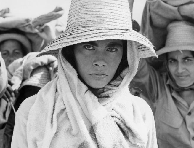 A woman in a straw hat stares directly at the camera in front of other women.