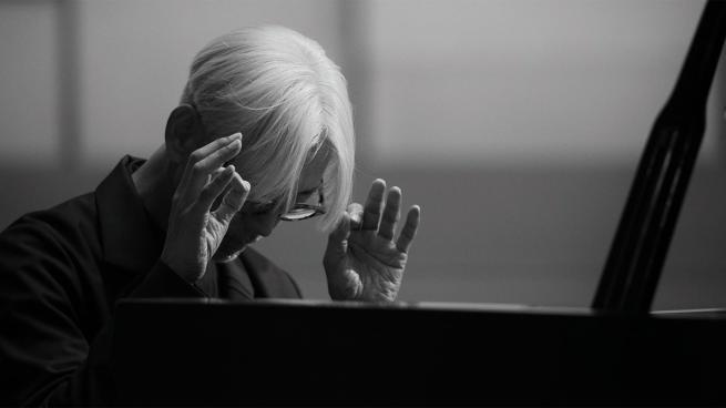 Black and white image of Ryuichi Sakamoto playing piano.