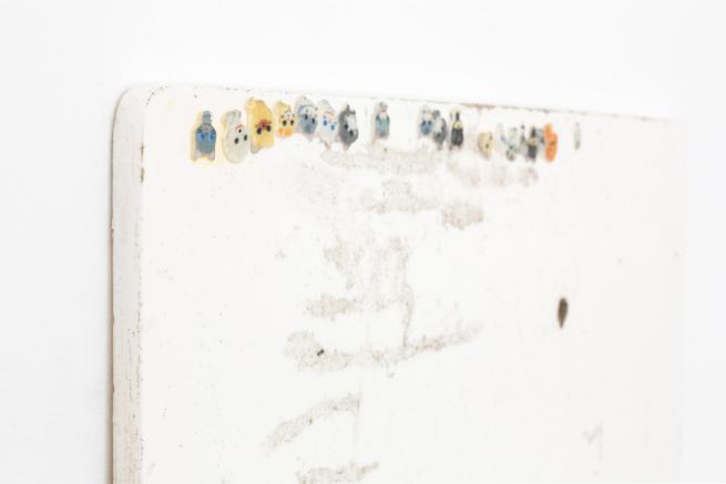 Close-up detail of a sculpture comprised of a piece of white board with upside-down stickers of cats on.