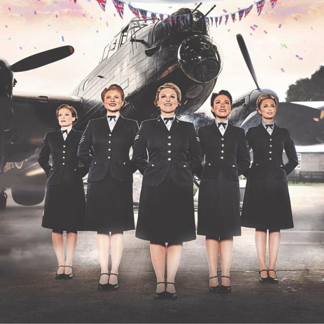 Five women in war-time military dress with their hands behind their backs stood in front of a fighter jet. Bunting appears at the top.