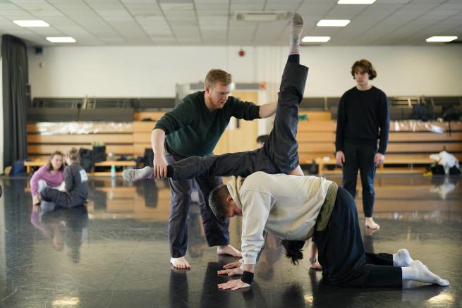 3 young people performing a lift in a dance studio with a black floor 