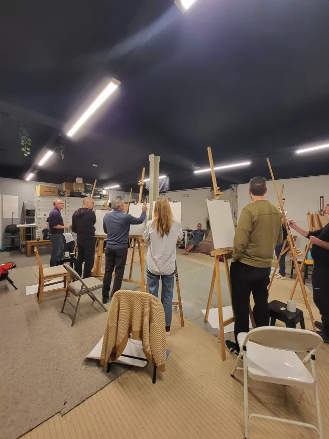 A group of artists standing at easels drawing a life model