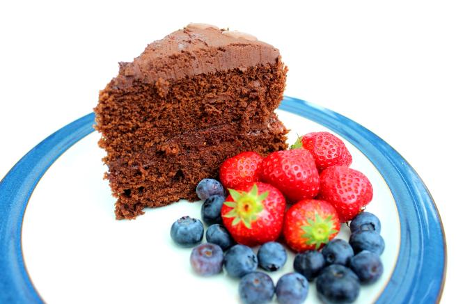 A blue and white plate with a large slice of chocolate cake, some strawberries and blueberries.