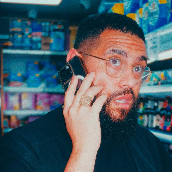 Grainy image of Jamali Maddix with his iPhone to his ear looking slightly shocked stood in the corner of a shop.