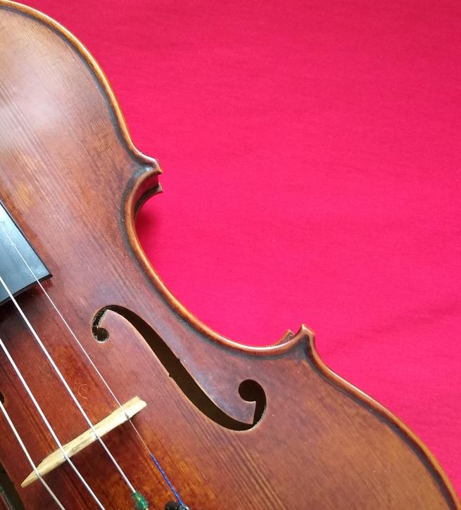 Part of a violin showing one f-hole and the bridge; on a bright red background