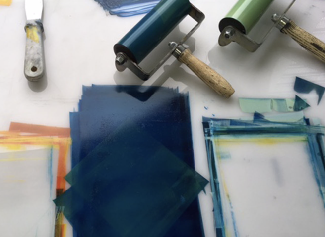 Ink rollers with green and blue inks being prepared on an acrylic surface.