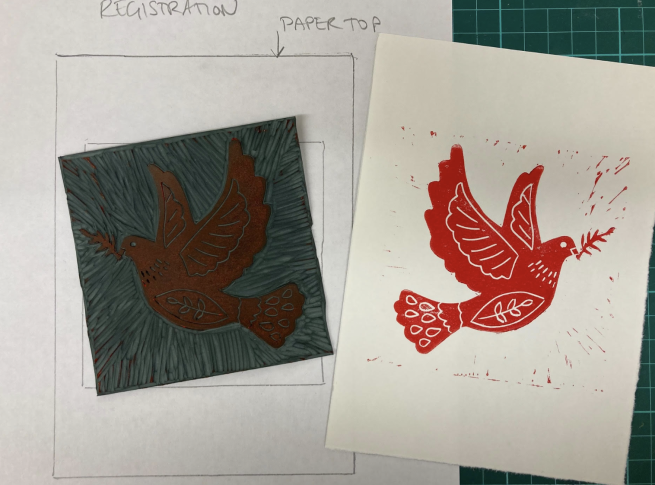 A lino printed dove in red ink, next to the piece of lino the print was taken from.