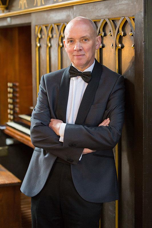 A man stood leaning against an organ. 