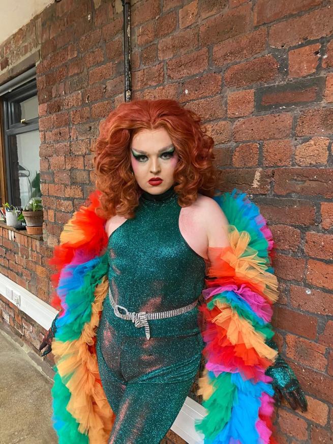 Pride Quiz Host and Drag Queen Sue Pertrouper wearing a fabulous outfirt and rainbow feather boa