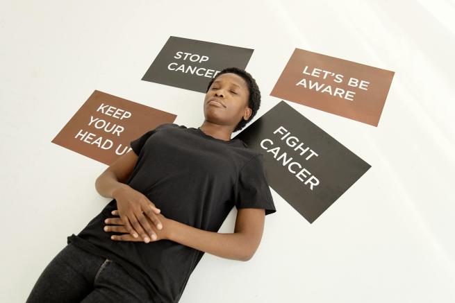 A person laying on the floor with signs around the topic of cancer around them