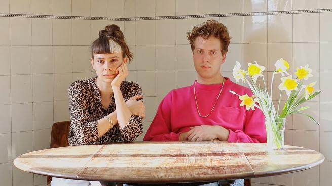 Swiss duo, Zimmerman and Lienhard, sit by a round coffee table, they're looking at the camera, looking like they haven't got anything to do, with an urge to do something