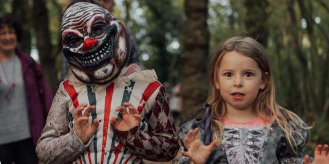 A child in a scary clown mask stands alongside a girl with fair hair in fancy dress, both grimacing