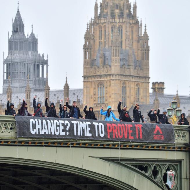 A photograph of some campaigners from the charity Shelter in front of the Houses of Parliament asking for a change of policy.