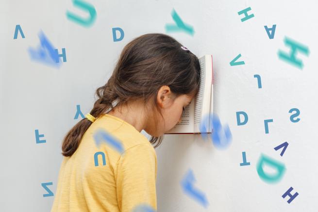 A defeated child with her head in a book against a wall with letters of the alphabet floating in the air