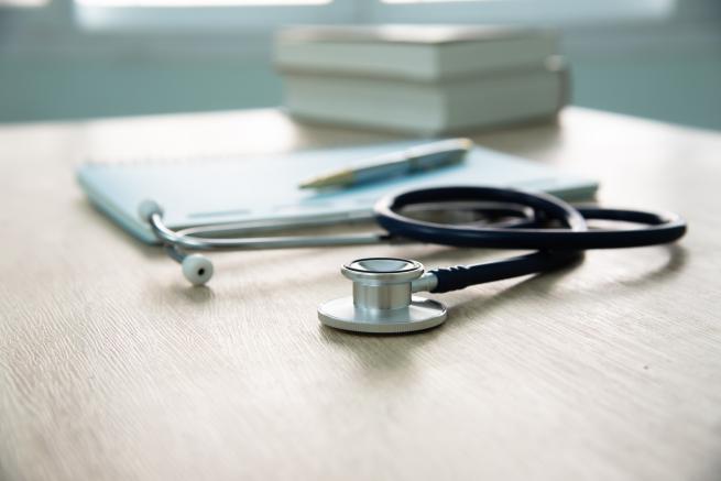 a clinical setting with stethoscope, paper, pen and books on a desk 