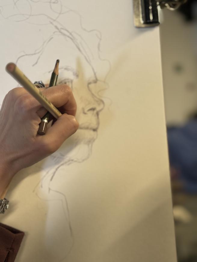 Close up image of a hand drawing a face with pencil