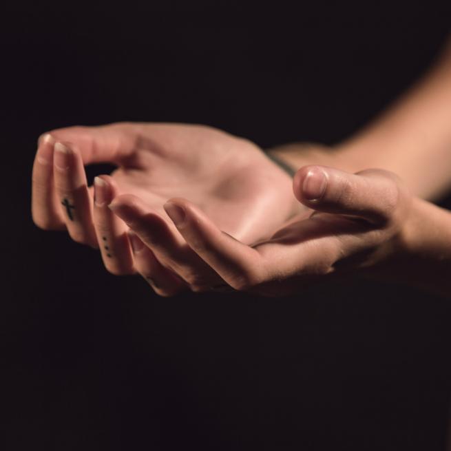 Two hands outstretched with palms facing up against a black background