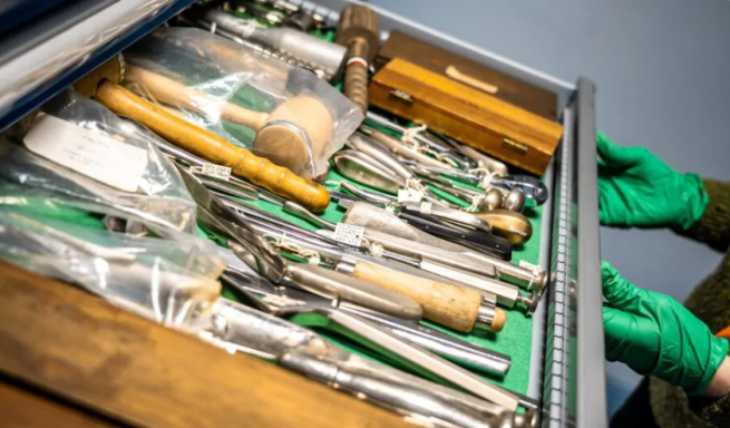 Two gloved hands opening a drawer of medical instruments.