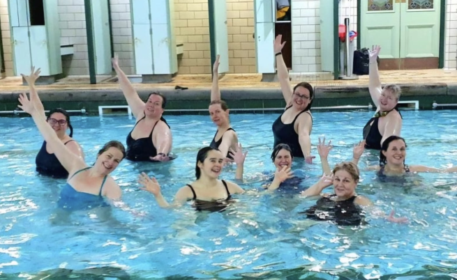 10 women and non binary people in water in bramley baths smiling arms raised