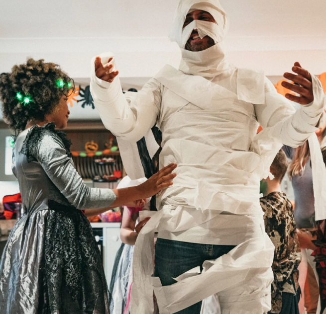 A picture of a man being wrapped in bandages by a child dressed as a witch