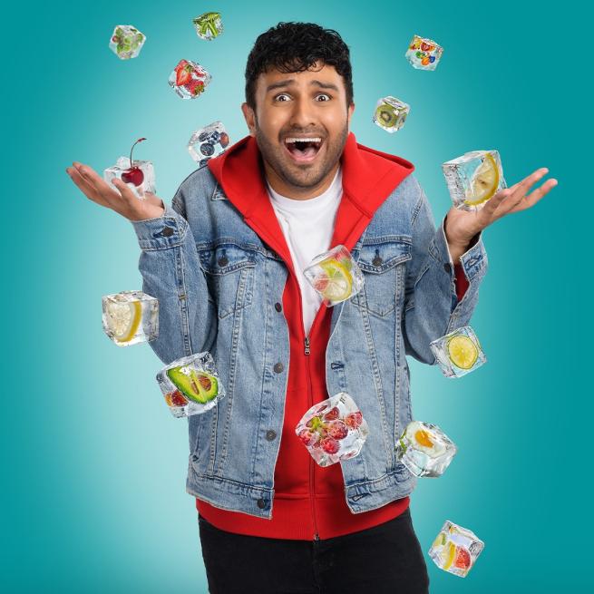 Shabaz Ali wearing a denim jacket over a red hoodie looking excited as ice cubes with fruit inside fall from the sky.