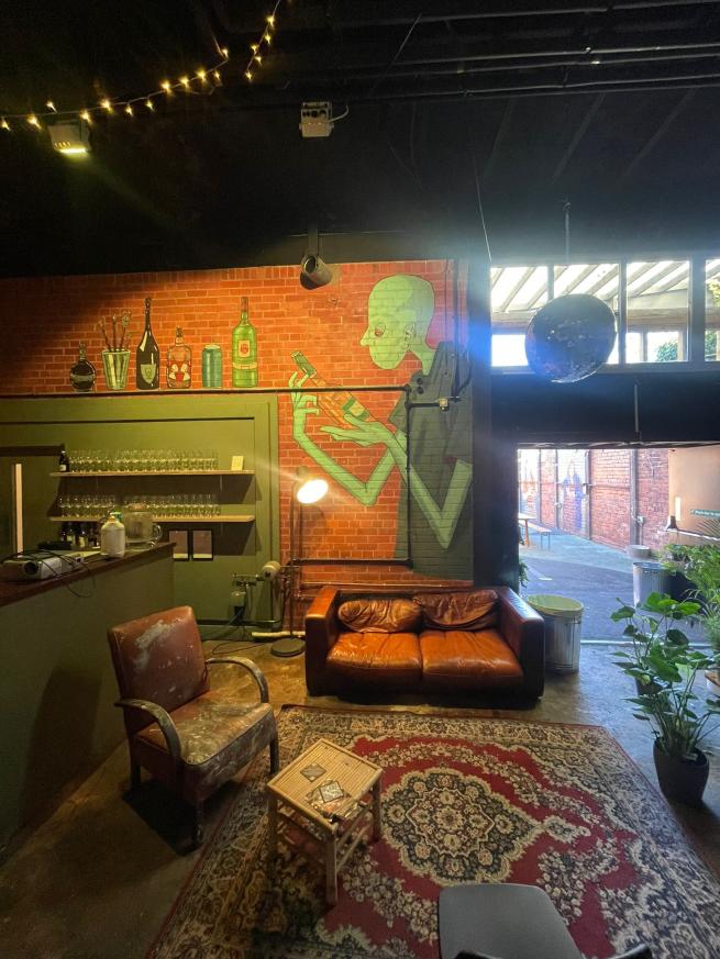 The image shows a corner of the Attic venue, next to the bar with sofas and a rug, disco balls and fairy lights and a colourful mural behind.