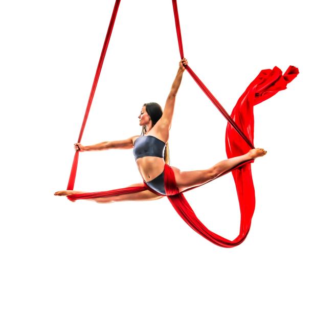 studio photo of Jess in sportswear for aerial silk against a blank background. She's held onto the silks whilst doing the splits in the air