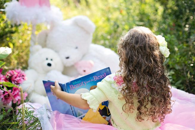 Little girl reading to a teddy in a garden