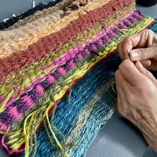 A woman's hands weaving wool into a colourful woollen blanket