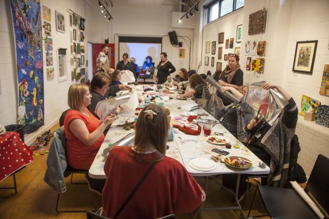 A room of people sat around a table creating art together 