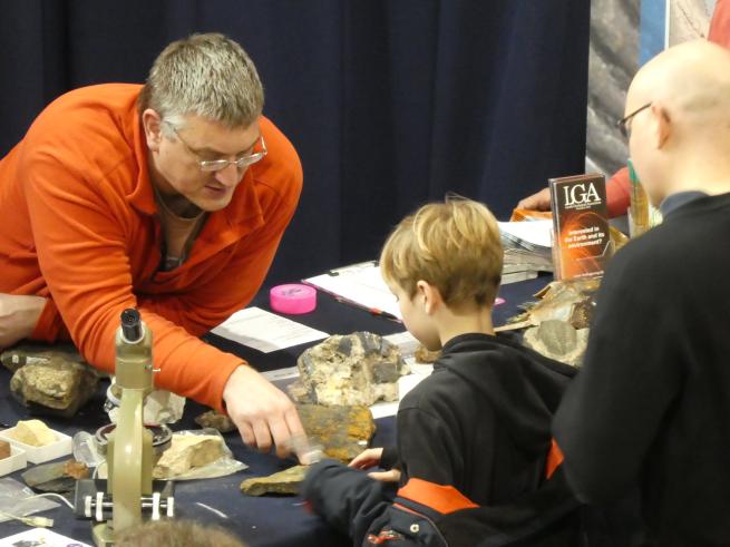 A man leaning over a table to show a young boy as fossil