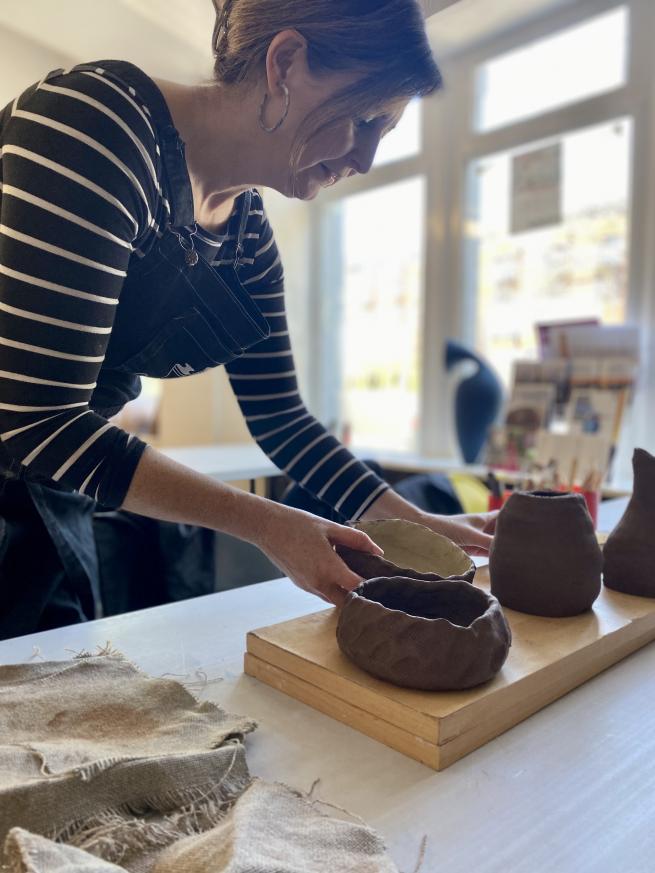 Jeannie a Leeds based pottery tutor arranges students clay pots on a board