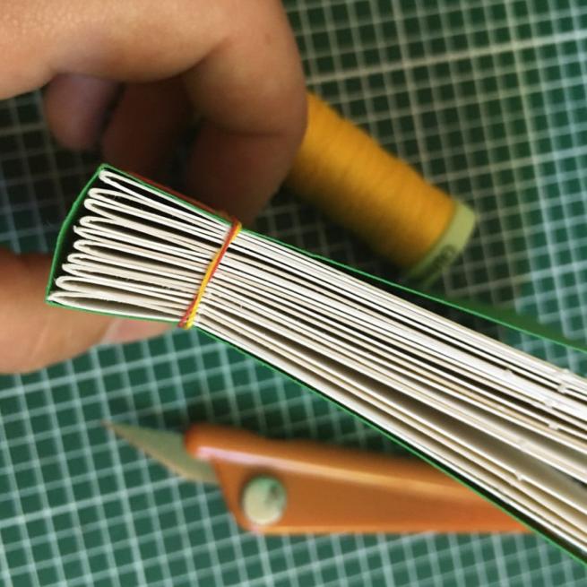 a hand holding a booklet that has yellow stitching